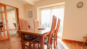 Uma área de refeições com uma mesa e cadeiras de madeira, uma janela com persianas e um relógio na parede.