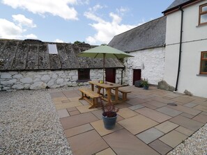 A patio with a wooden table and benches, a green umbrella, and a potted plant. - Maerdy Cottage (Corwen)