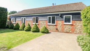 A two-story house with a tiled roof, stone and brick walls, and a paved driveway. - The Meadows Cottage (Dereham)