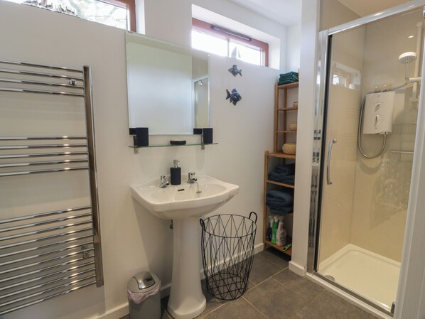 A bathroom with a white sink, mirror, and glass shower enclosure. - The Garden House (Duns)