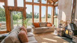 A spacious living room with a large window, a sofa, a rug, and a wood-burning stove. - The Tractor Shed (Shrewsbury)