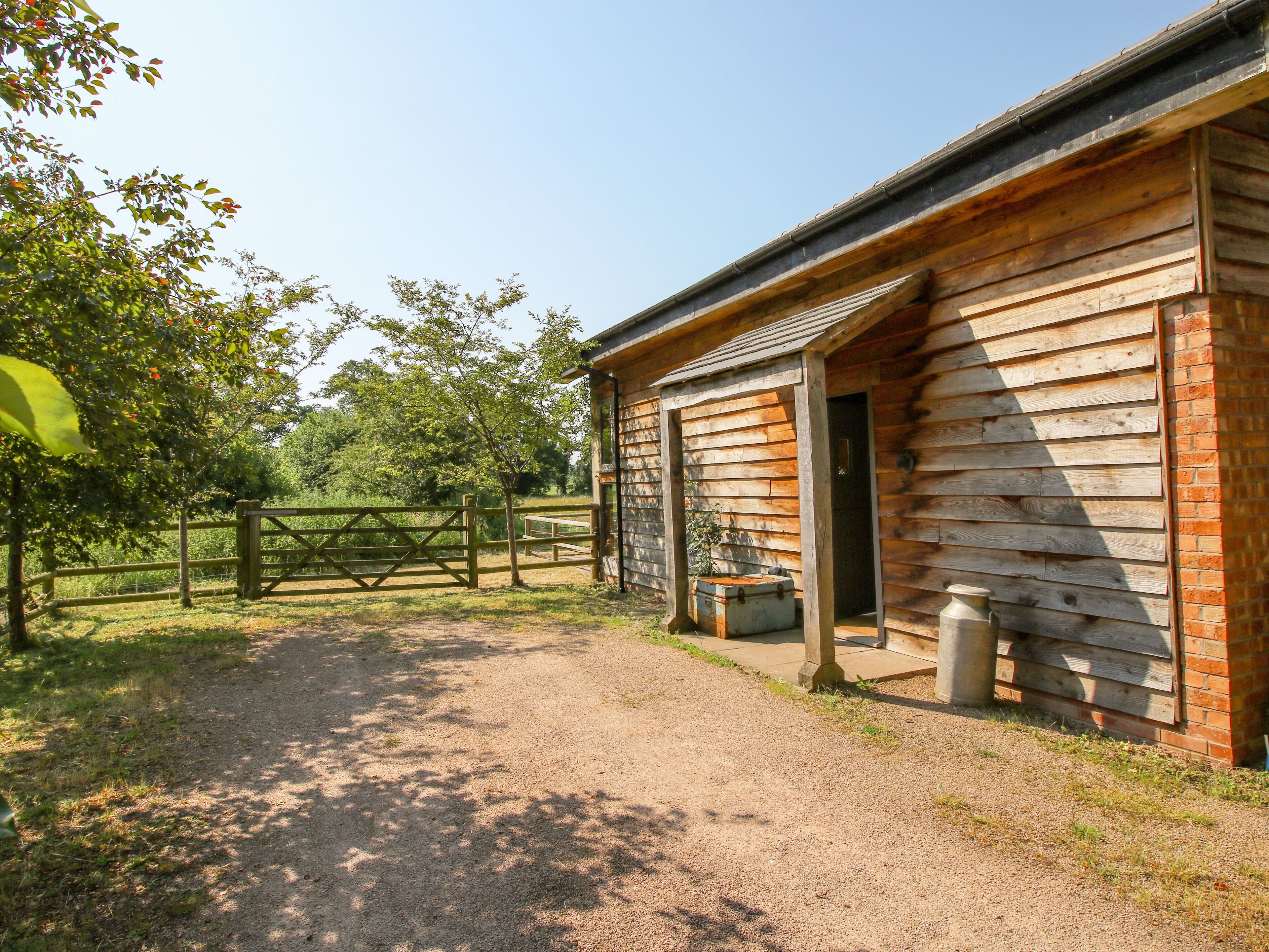 A rustic wooden building with a gravel path leading to it, surrounded by trees and a wooden fence.