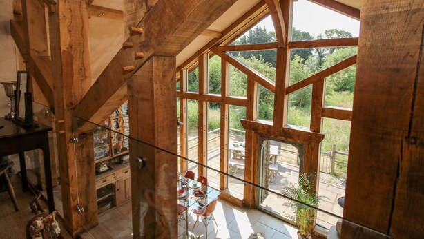 A spacious room with a high ceiling and large windows, wooden beams, a dining area with a table and chairs, and a view of the outdoors. - The Tractor Shed (Shrewsbury)