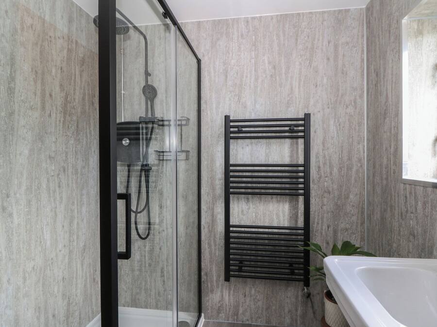 A modern bathroom with a glass-enclosed shower, a black towel rack, and a white bathtub.