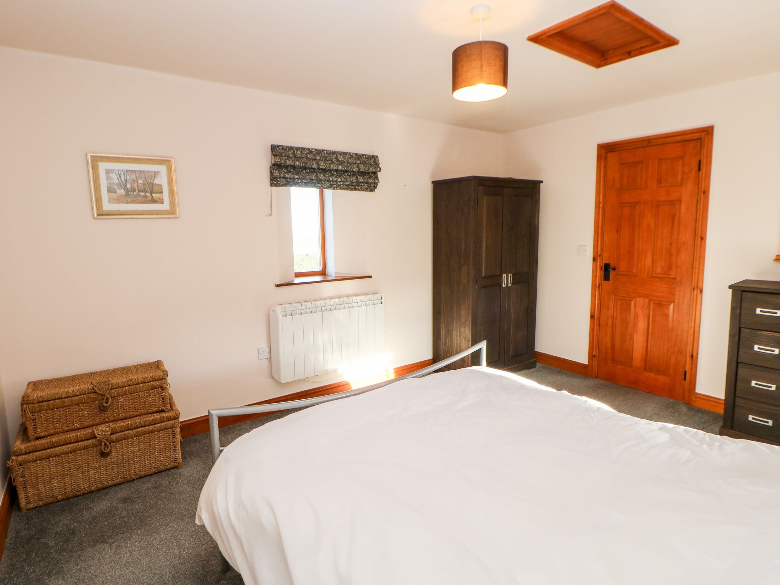Een slaapkamer met een bed, een kledingkast, een radiator, een raam met gordijn, een foto aan de muur en een houten deur.