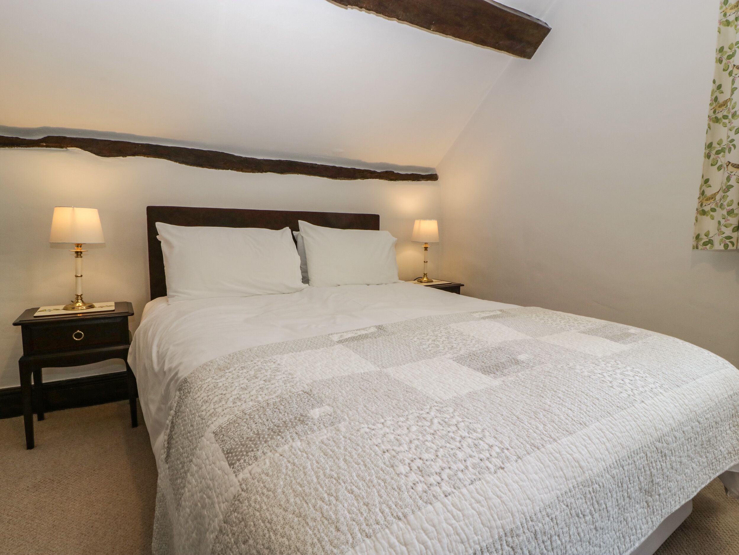 A neatly made bed with a quilt, two bedside tables with lamps, and a wooden beam above the bed.