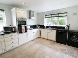 A modern kitchen with white cabinets, a built-in oven, a microwave, a dishwasher, and a window with blinds.