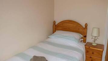 A single bed with a wooden headboard, a bedside table with a lamp, and a folded towel on the bed.