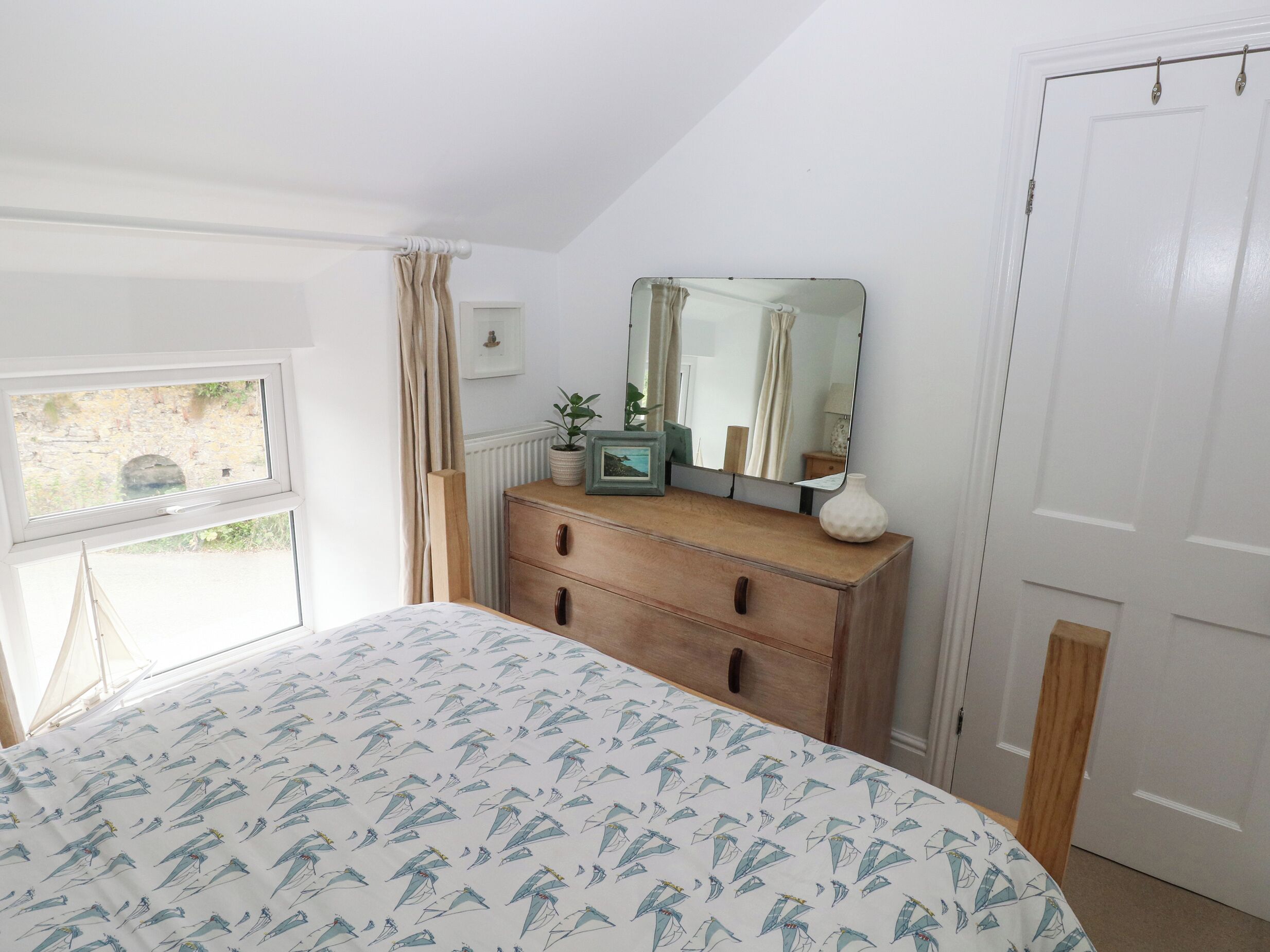 A bedroom with a bed, a dresser, a mirror, and a window.