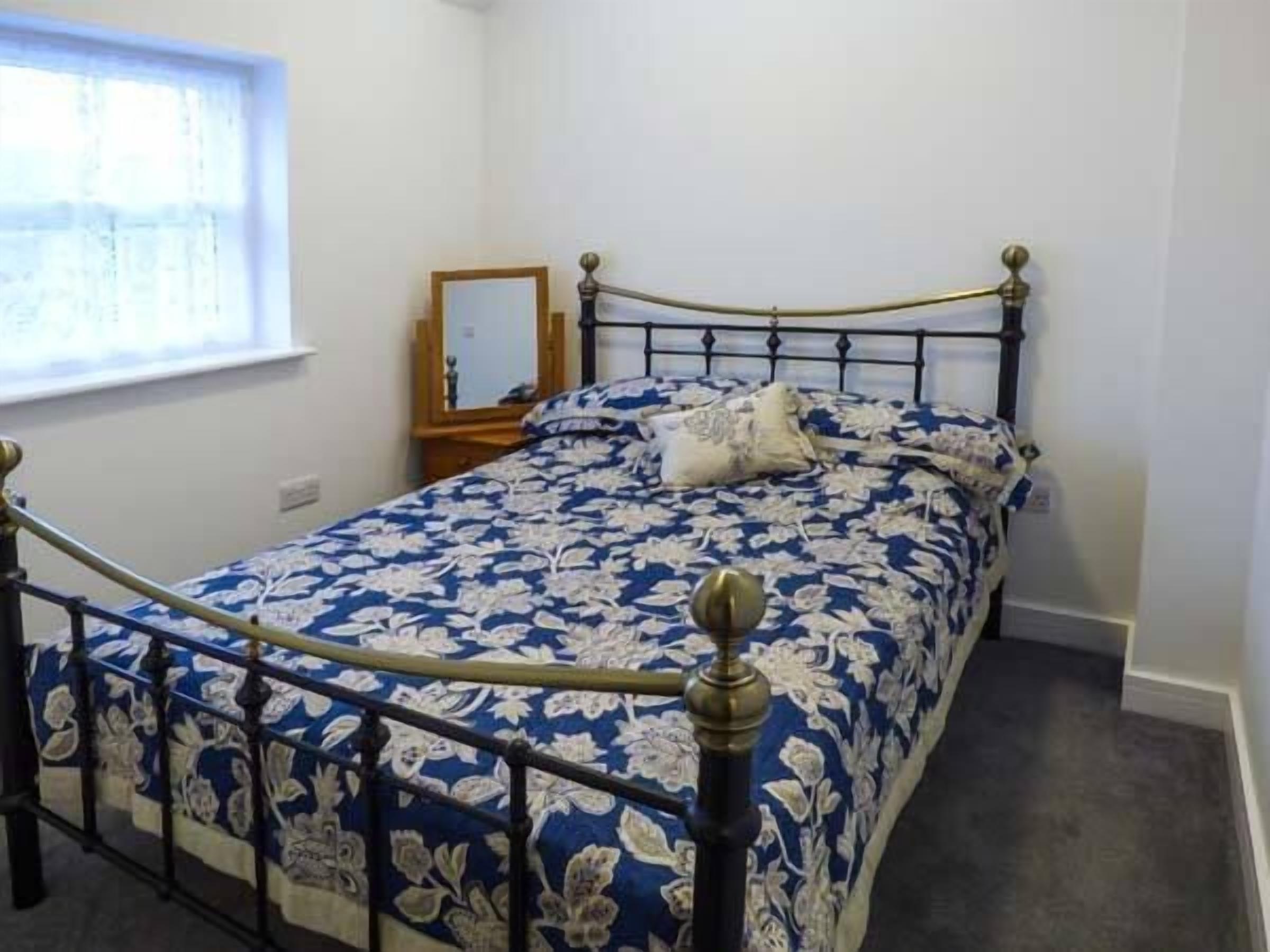 A bedroom with a bed, a nightstand, a mirror, and a window.