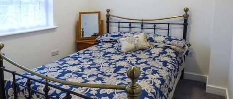 A bedroom with a bed, a nightstand, a mirror, and a window.