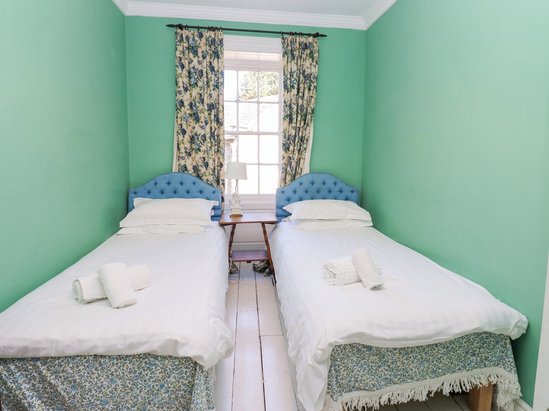 A room with two beds, each with a blue headboard, white bedding, and a small table between them.
