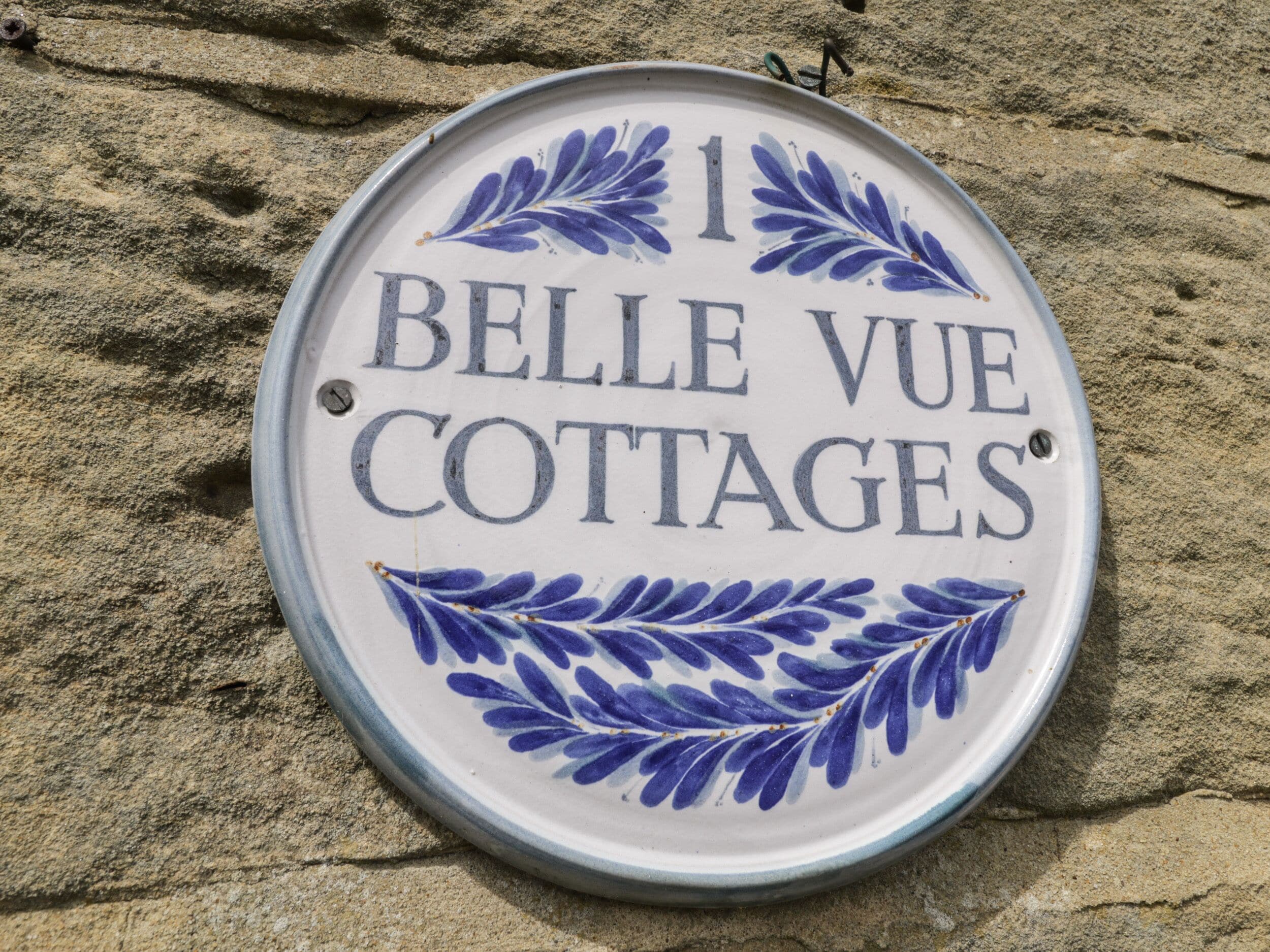 A sign for "Belle Vue Cottages" with decorative blue floral patterns.