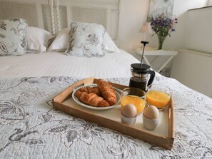 A neatly made breakfast tray with croissants, eggs, and orange juice on a bed with a floral-patterned bedspread. - 1 Belle Vue (Northallerton)