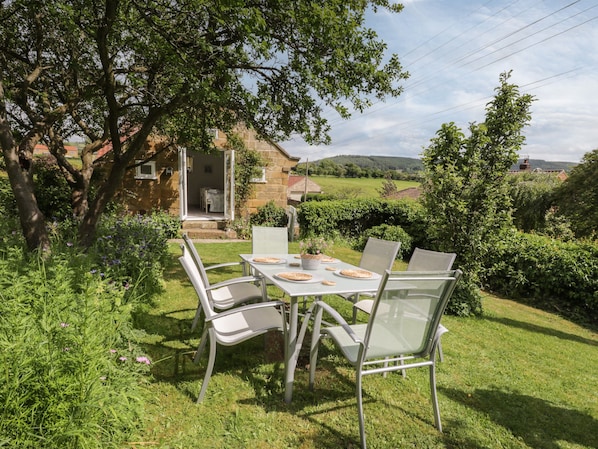 Un patio giardino con tavolo e sedie, immerso nel verde e affiancato da un edificio in pietra.