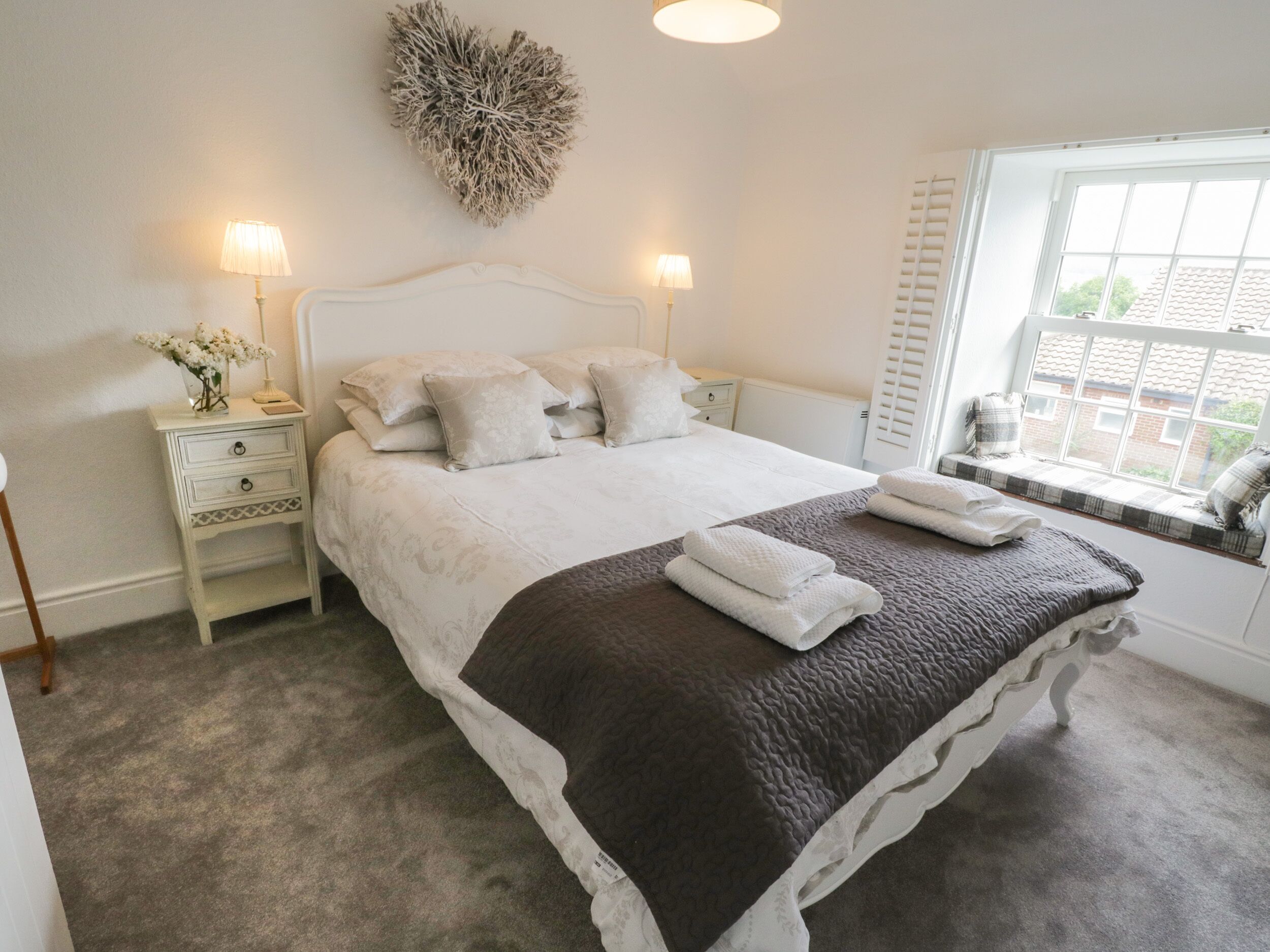 A neatly arranged bedroom with a bed, bedside tables, lamps, and a window with a view.