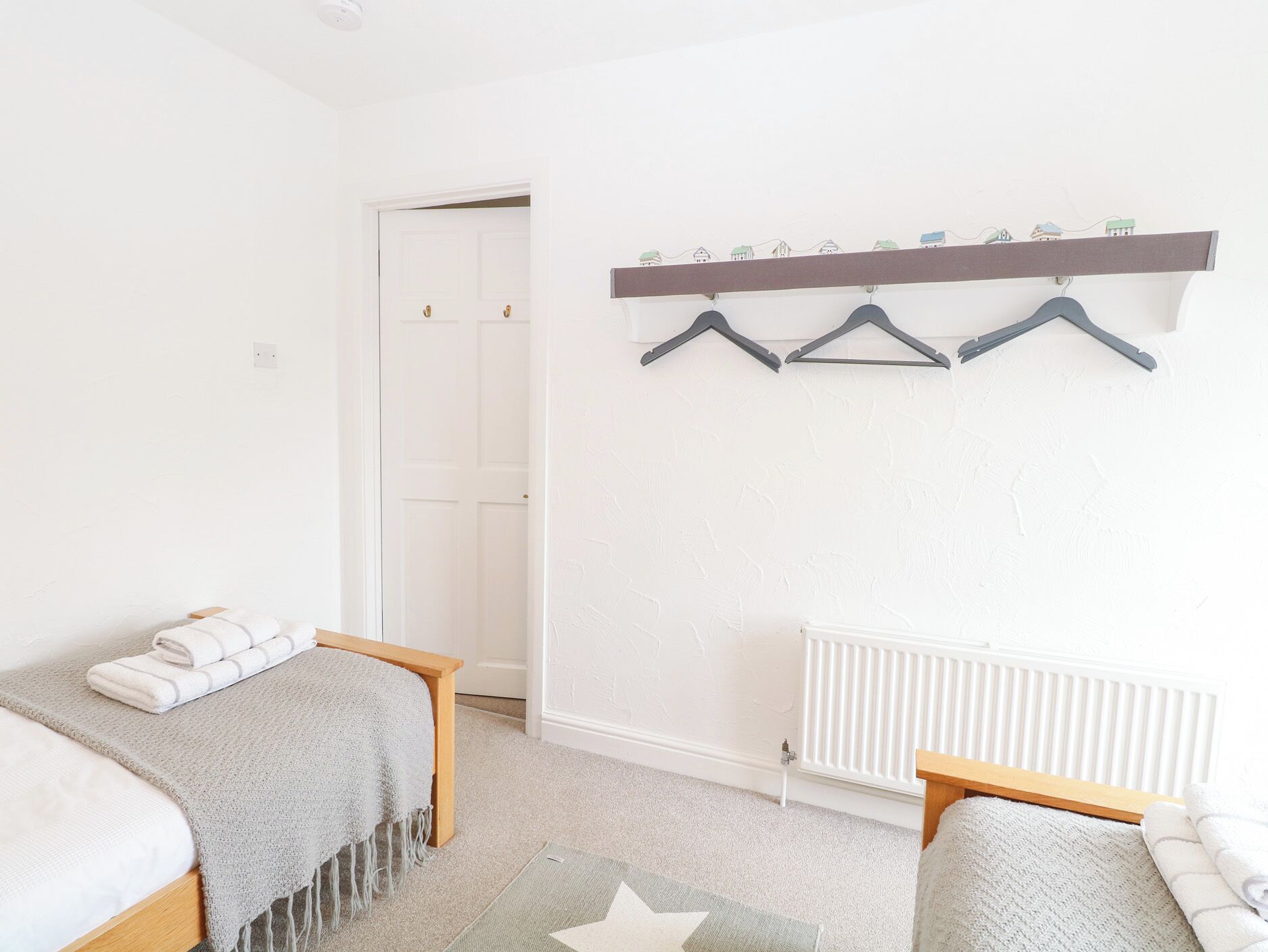 A bedroom with two beds, a radiator, a coat rack with hangers, and a star-patterned rug.