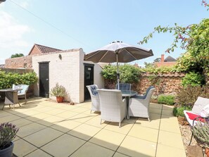 A patio with wicker furniture, a table, and an umbrella. There is a brick wall and a door to a building.