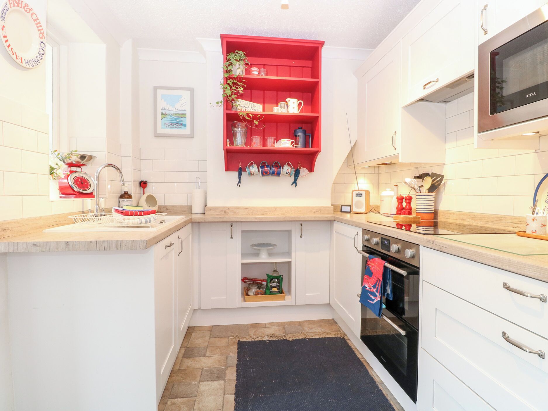 A compact kitchen with white cabinets, a red shelf, a microwave, and a small oven.