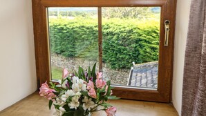 A wooden-framed window with a view of a stone wall and greenery outside. - The Barn Cottage (Hexham)