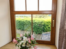 Una ventana con marco de madera que ofrece vista a un muro de piedra y follaje.