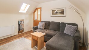 A cozy living room with a grey sofa, a small wooden table, a bookshelf, and a framed picture on the wall. - Shephards Retreat (Somerton)