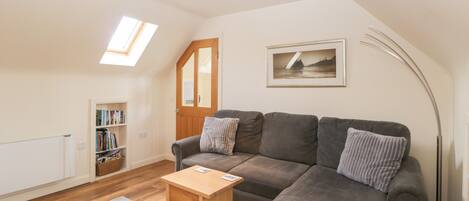 A cozy living room with a grey sofa, a small wooden table, a bookshelf, and a framed picture on the wall.