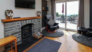 Una sala de estar con chimenea de piedra, televisor montado, un sillón de cuero cómodo y vistas a un patio exterior a través de puertas correderas de vidrio.