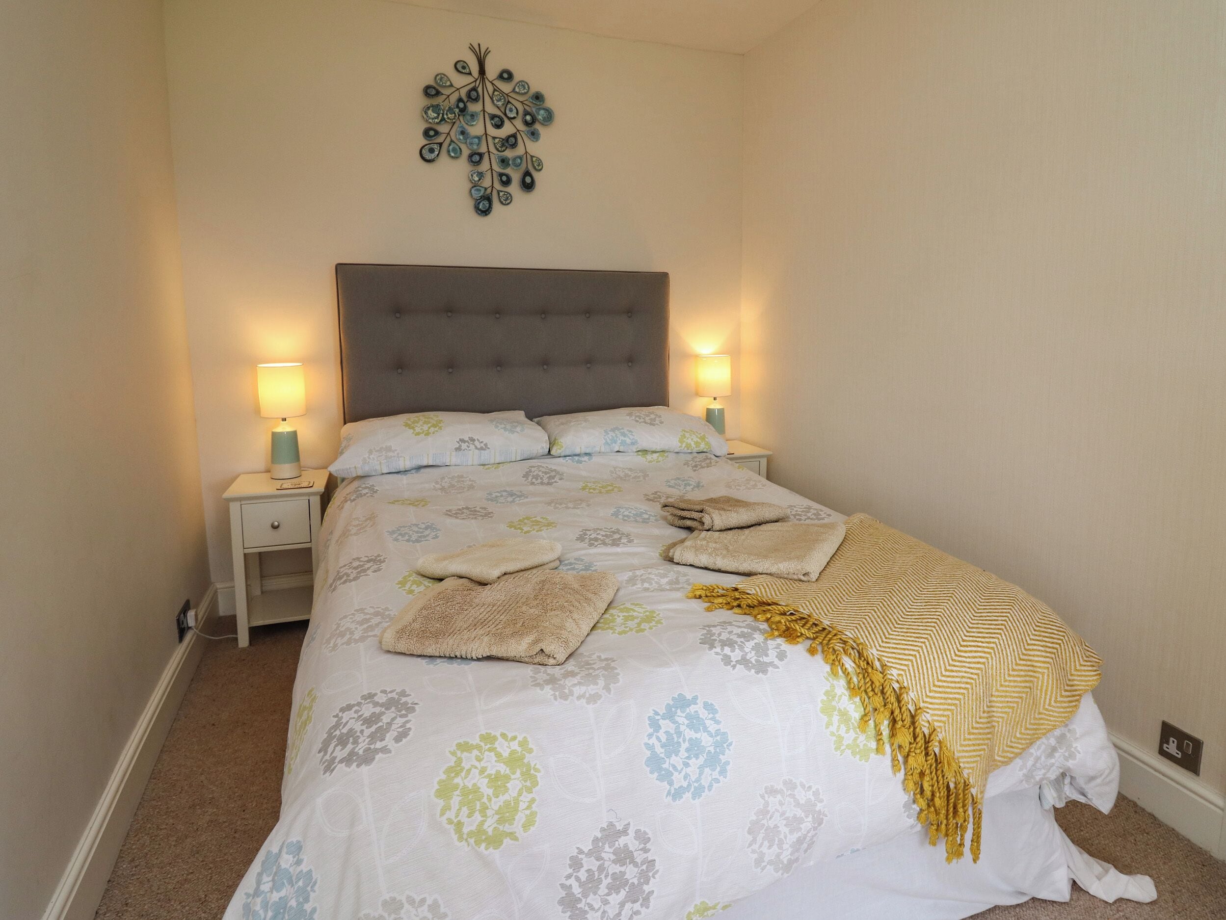 A neatly made bed with a floral-patterned bedspread, two bedside lamps, and a decorative wall piece above the bed.