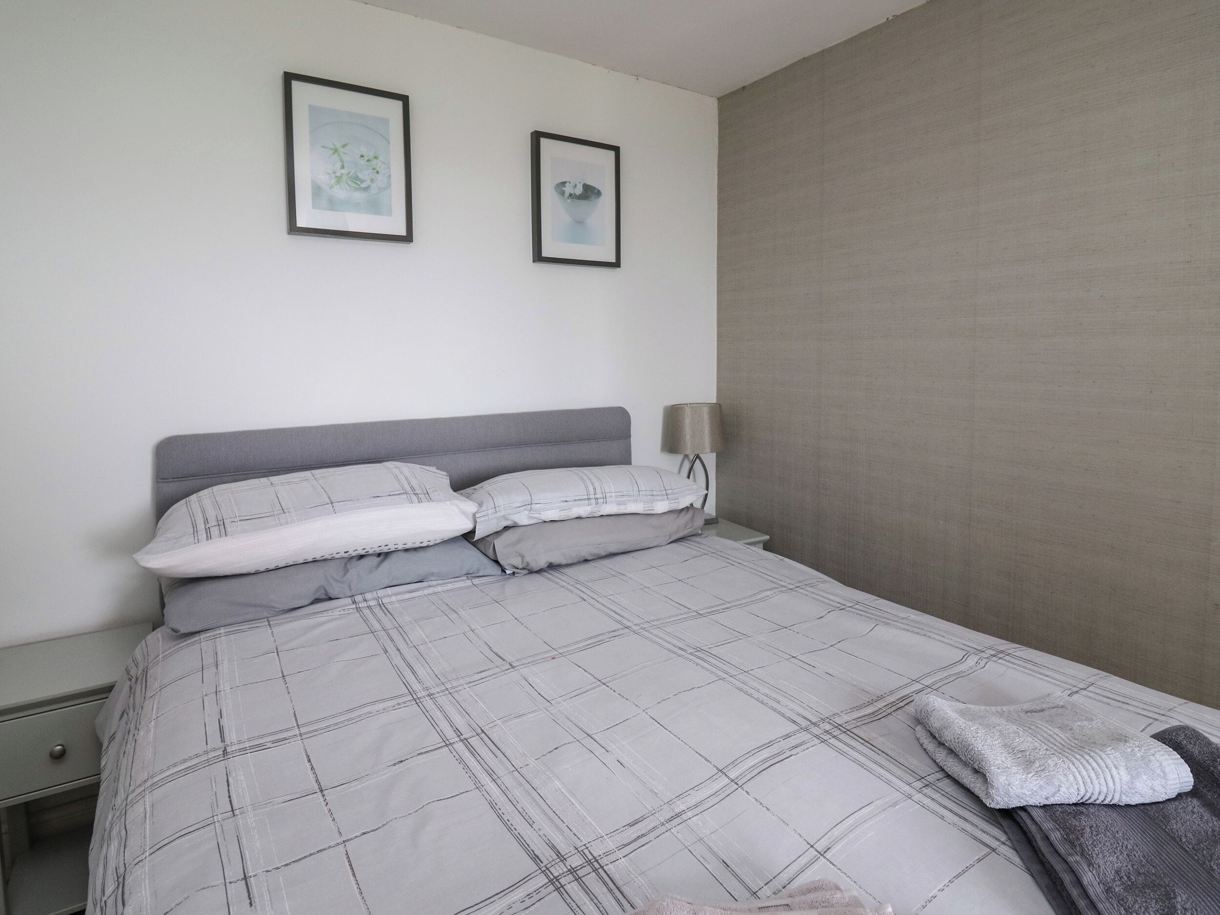 A neatly made bed with a plaid bedspread and two pillows, a bedside lamp, and two framed pictures on the wall.