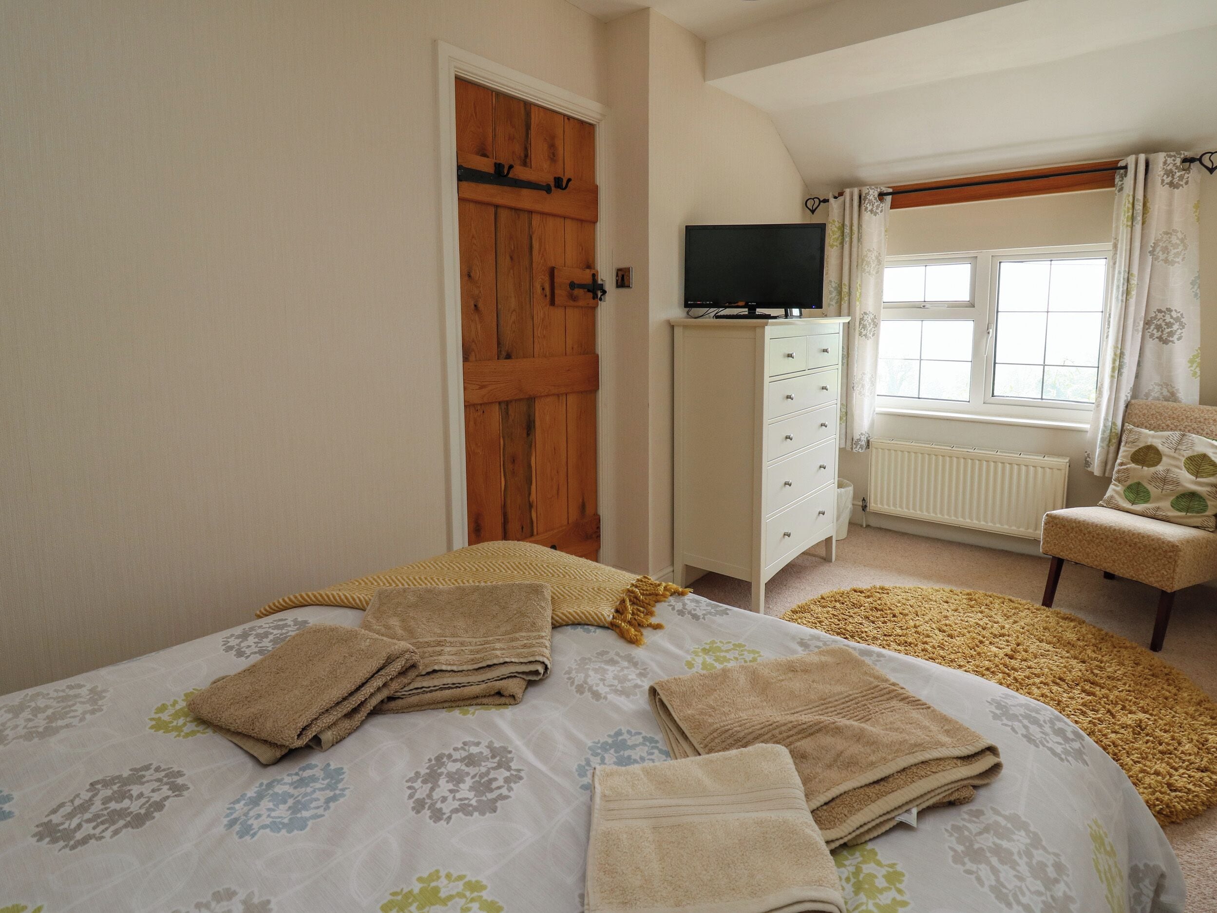 A bedroom with a bed, a dresser, a television, a window with curtains, and a chair.