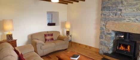 A cozy living room with a stone fireplace, wooden beams, and two lamps.