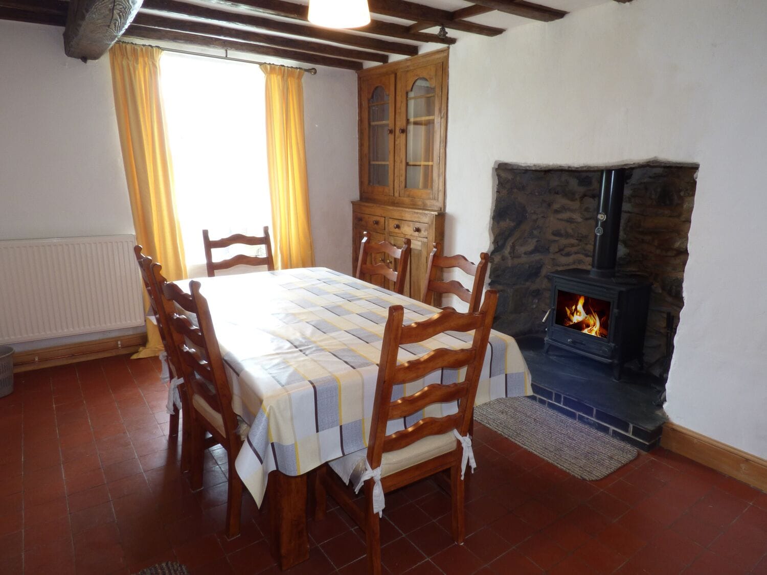 A dining room with a table set for four, wooden chairs, a cabinet, and a stone fireplace with a wood-burning stove.