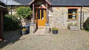 A stone cottage with a wooden door, a gravel driveway, and potted plants. - Sandpiper Cottage (Whitland)