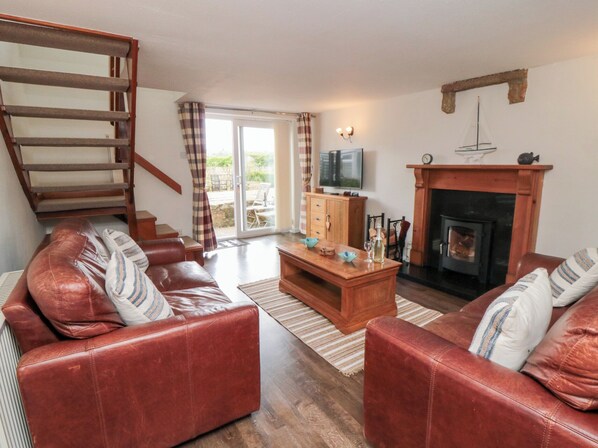 A living room with a fireplace, leather sofas, a wooden coffee table, and a television. - Fairhaven Cottage (Whitby)
