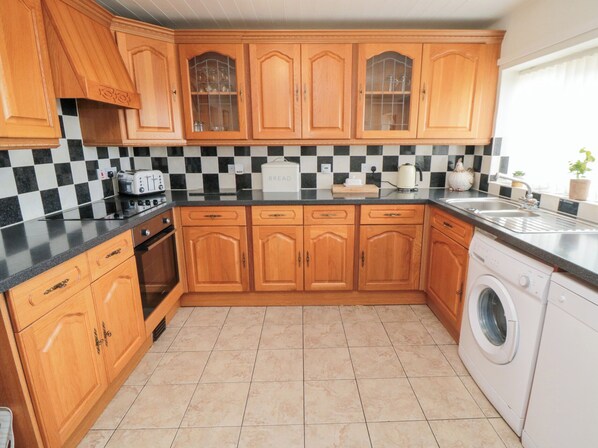 A kitchen with wooden cabinets, a checkered backsplash, a washing machine, and a toaster. - Fairhaven Cottage (Whitby)