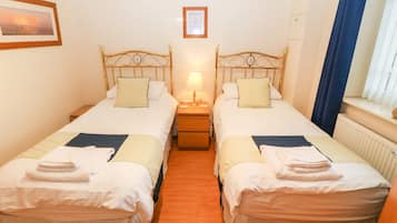 A twin room with two single beds, a nightstand with a lamp, a framed picture on the wall, and a window with curtains.