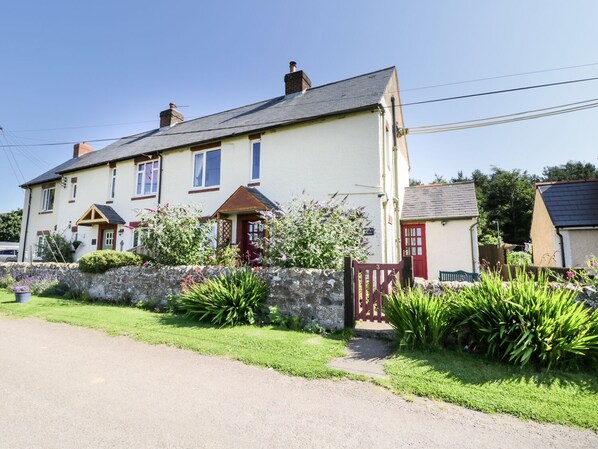 A two-story house with a stone wall, a red gate, and a well-maintained garden. - Bunty's Place (Alnwick)