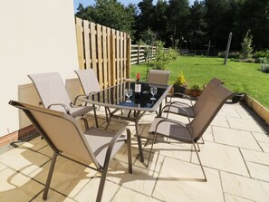 An outdoor patio with a glass-top table and four chairs, surrounded by a wooden fence and a grassy lawn. - Bunty's Place (Alnwick)