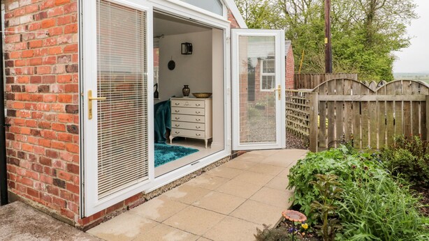A small, brick house with a sliding glass door leading to a bedroom. - St Cuthbert's Cottage (Berwick-upon-Tweed)