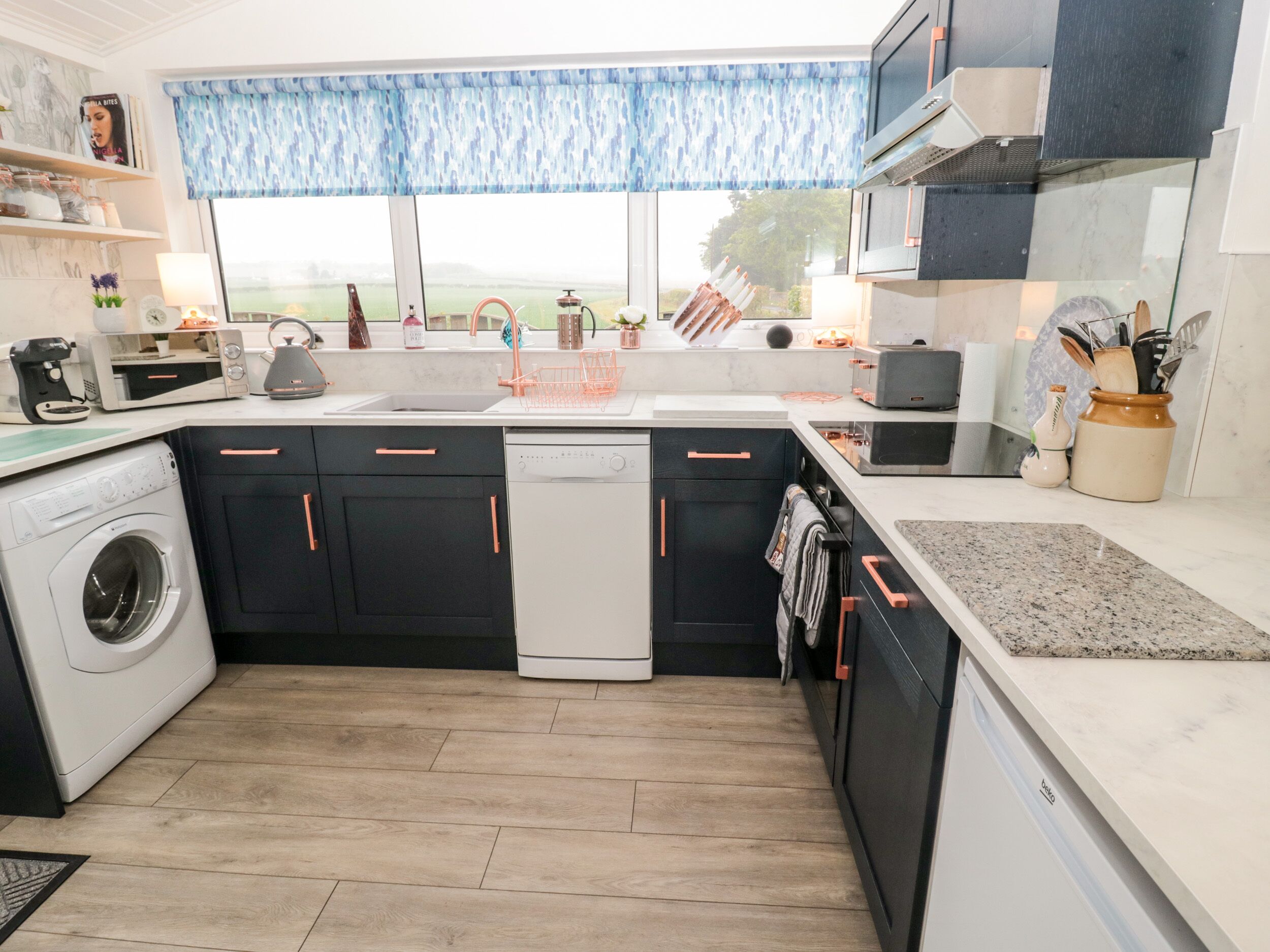 A modern kitchen with a washing machine, dishwasher, and a large window with a view of the outdoors.