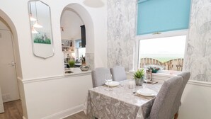 A dining area with a table set for four, a mirror on the wall, and a window with a view of a wooden deck. - St Cuthbert's Cottage (Berwick-upon-Tweed)