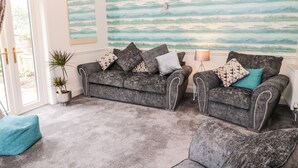 A living room with two grey upholstered sofas, a teal pouf, and a large abstract mural on the wall. - St Cuthbert's Cottage (Berwick-upon-Tweed)
