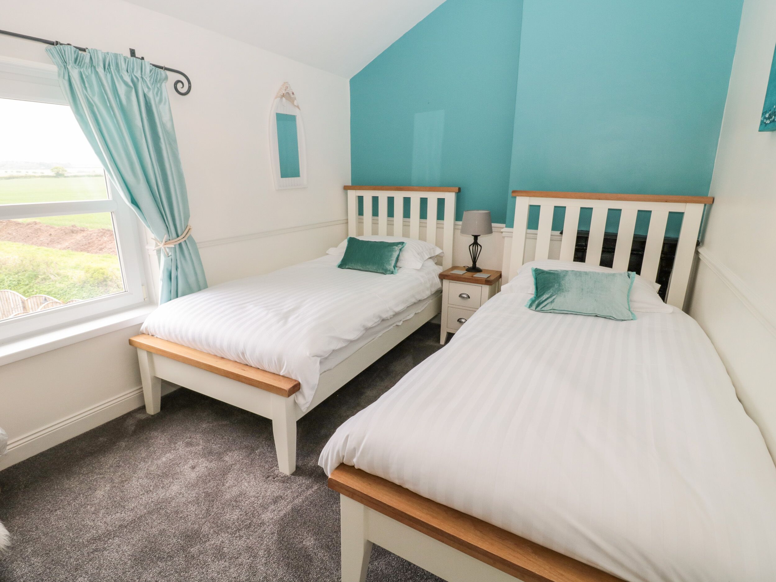 Un dormitorio con dos camas individuales, una ventana con cortinas, una mesita de noche con lámpara y vistas al exterior.