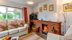 A cozy living room with a fireplace, a sofa, a television, and a window with curtains. - The Olde House (Ross-on-Wye)