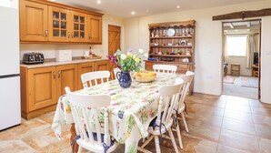 A kitchen with wooden cabinets, a dining table with chairs, a vase with flowers, and a bookshelf. - Bodywen (Oswestry)