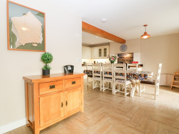 A modern kitchen with wooden cabinets, a dining area with white chairs, and a herringbone-patterned floor. - Ty Top (Holyhead)
