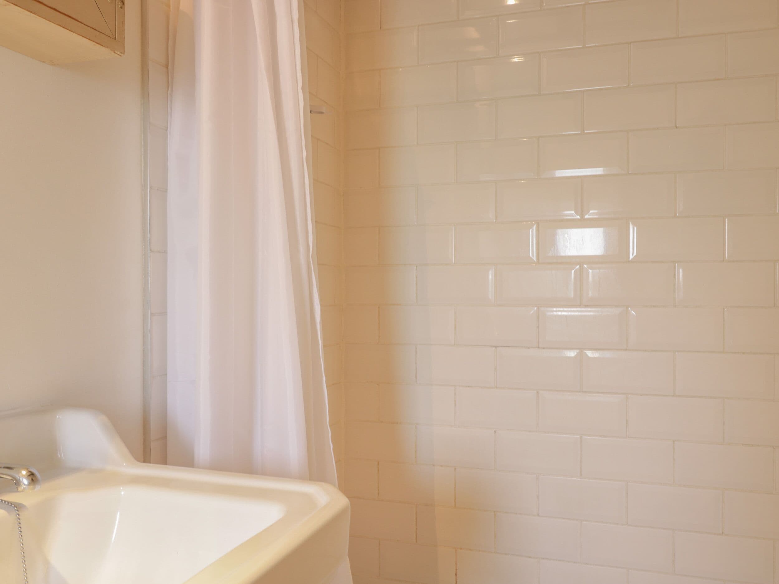 Un baño con lavamanos blanco, cortina de ducha y pared con azulejos.