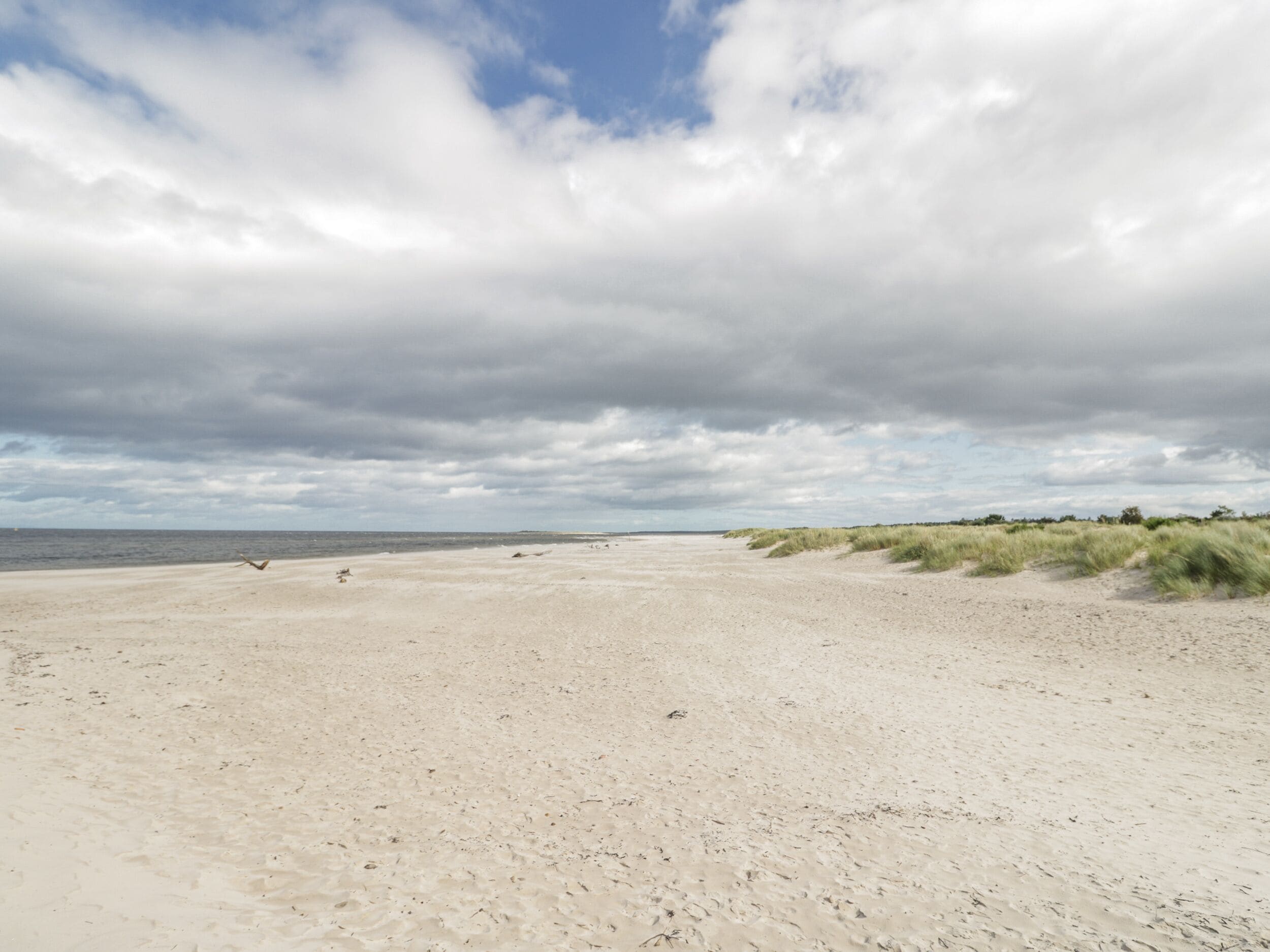 Una playa arenosa con dunas y cielo nublado.