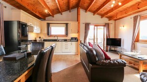 Una cocina moderna con vigas de madera, un comedor con sofá de cuero negro y una sala de estar con televisor de pantalla plana.